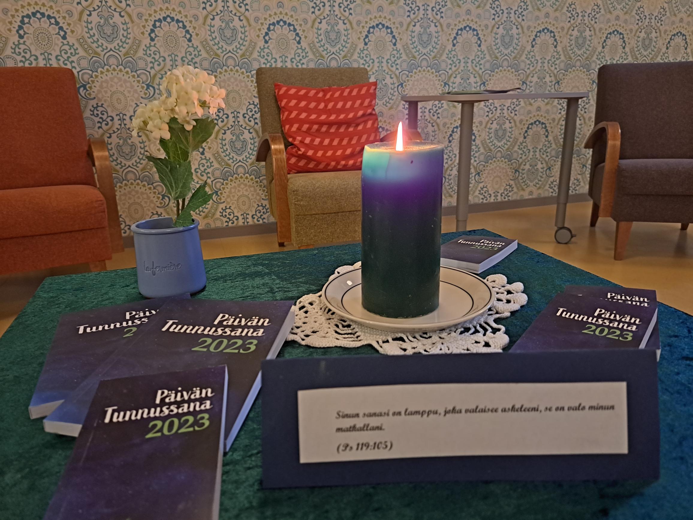 Pöydällä kynttilä, kukka ja Päivän Tunnussana -kirjoja.