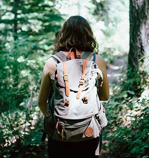 Nainen kävelee metsässä reppu selässään.